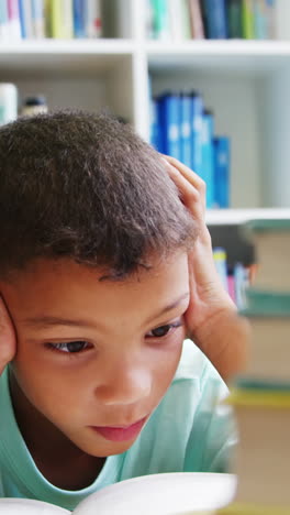 Schoolboy-reading-book-in-library-at-school