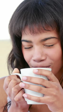 Smiling-woman-drinking-hot-beverage-on-bed