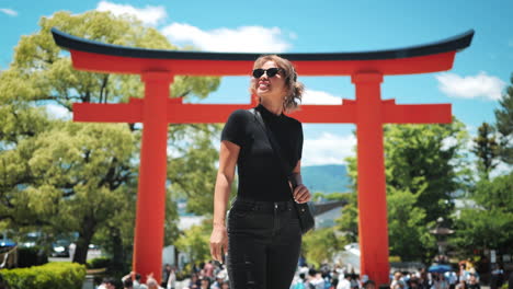 Smiling-woman-posing-with-sunglasses-in-front-of-a-red-torii-gate,-dressed-in-black