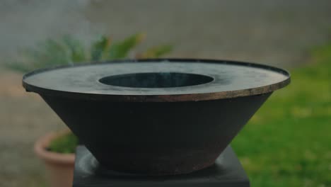 Close-up-of-smoke-rising-from-a-round-outdoor-wood-grill-in-a-garden-setting