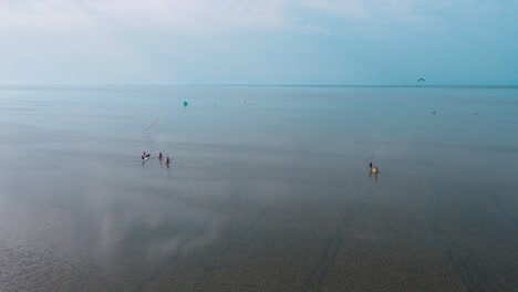 Vista-Aérea-De-Una-Playa-Con-Varios-Remeros-Caminando-En-Una-Playa-Tranquila-Con-El-Reflejo-De-La-Laguna-De-Djerba-En-Túnez,-El-Ambiente-General-Parece-Ser-Relajado-Y-Pausado.