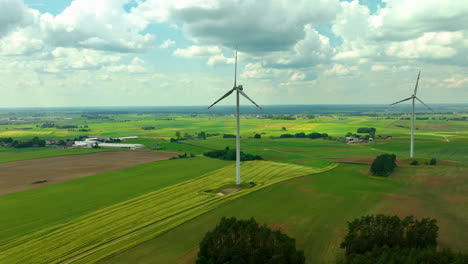 Aerial-footage-featuring-two-wind-turbines-in-a-vast-green-agricultural-landscape