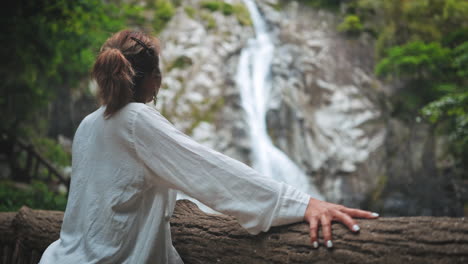 Woman-stands-at-the-edge-of-waterfall,-admiring-the-natural-spectacle,-surrounded-by-lush-vegetation