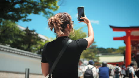 Woman-with-curly-hair-in-a-black-outfit-drinks-a-beverage-while-standing-in-front-of-a-Japanese-shrine