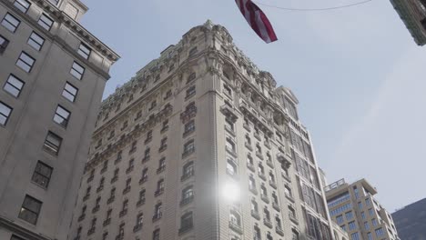 Schwenken-Von-Einer-Im-Wind-Wehenden-Amerikanischen-Flagge-Auf-Ein-Kunstvolles-Gebäude-Mit-Klassischer-Architektur,-An-Dessen-Eingang-Ebenfalls-Eine-Amerikanische-Flagge-Weht,-In-New-York-City,-New-York