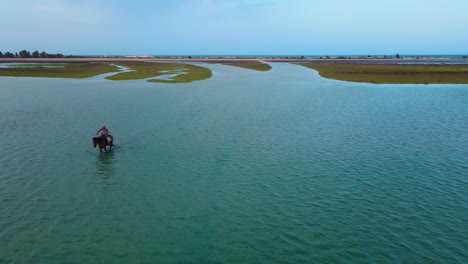 Eine-Luftaufnahme-Einer-Frau,-Die-Auf-Einem-Pferd-Durch-Das-Seichte-Wasser-Der-Lagune-Von-Djerba-In-Tunesien-Reitet