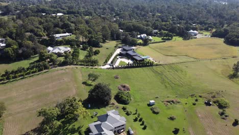 Drone-flying-towards-large-Australian-countryside-private-properties-with-swimming-pools-and-solar-panels-surrounded-with-nature