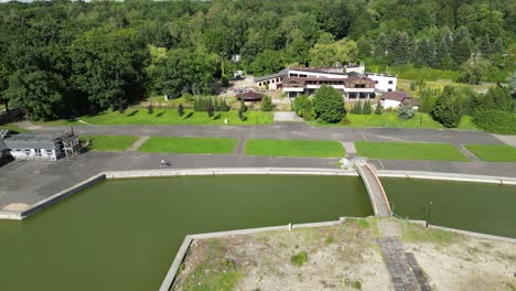 Park-with-pond-during-a-beautiful-summer-day-surrounded-by-lush-greenery,-grass,-and-trees-under-a-clear-blue-sky