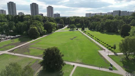 Park-during-a-beautiful-summer-day-surrounded-by-lush-greenery,-grass,-and-trees-under-a-blue-sky-with-buildings-in-the-distance