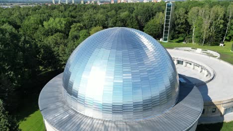 Great-planetarium-during-a-beautiful-summer-day,-surrounded-by-lush-greenery,-grass,-and-trees-under-a-clear-blue-sky