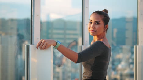 Woman-dressed-in-a-grey-top,-reflects-over-a-bustling-cityscape-from-a-glass-railing