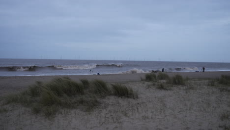 Strandszene-In-Der-Abenddämmerung-Zeigt-Ein-Paar-Fischer-Am-Ufer,-Die-Ihre-Ruten-Vor-Dem-Hintergrund-Sanfter-Wellen-Ausbreiten