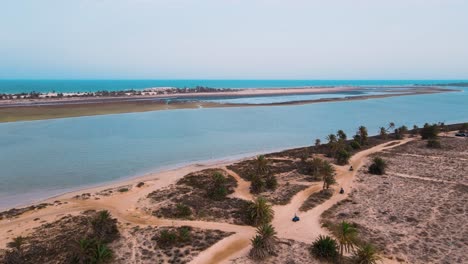 Eine-Luftaufnahme-Eines-Strandes-Mit-Sichtbarem-Meer-Und-Sandstrand-In-Der-Lagune-Von-Djerba-In-Tunesien,-ATV-Quad-Auf-Einem-Feldweg,-Der-Durch-Das-Gebiet-Führt