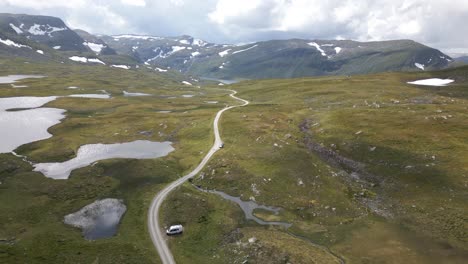 Aerial-drone-shot-following-a-long-gravel-trail-on-top-of-Vikafjellet-in-Norway,-eventually-revealing-a-large-lake-on-top-of-the-mountain