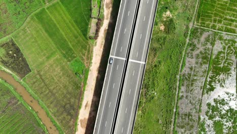 Embark-on-a-mesmerizing-journey-as-the-drone-vertically-descends,-capturing-the-serene-beauty-of-Sri-Lanka's-paddy-fields-and-modern-expressways-from-above