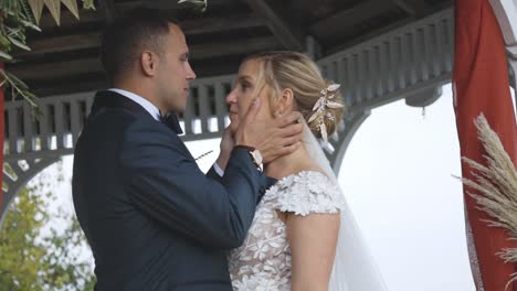 Groom-kisses-bride-on-forehead-under-Gazebo