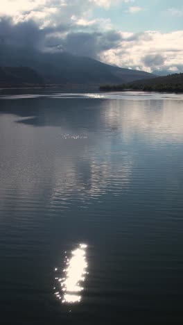 Vista-Aérea-Vertical-Del-Hermoso-Lago-Alpino-Y-Montañas,-Nubes-Y-Reflejo-Del-Cielo-En-La-Superficie-Del-Agua