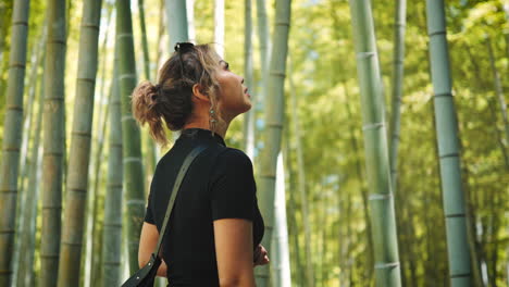 Woman-exploring-a-bamboo-forest,-looking-upwards-with-a-sense-of-wonder