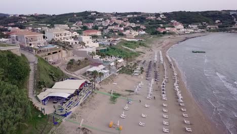 Aerial-drone-view-of-a-Greek-beach,-descending-to-show-empty-beach-and-sun-loungers-late-evening