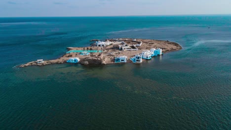 Una-Vista-Aérea-De-La-Isla-El-Biben-Con-Una-Piscina-Y-Casas-De-Acogida-Se-Encuentra-En-Medio-Del-Océano-Con-Palmeras,-Rodeada-De-Agua-Creando-Una-Hermosa-Atmósfera