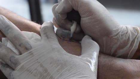 Extreme-Close-up-Of-Tattooist-Hands-Holding-Tool-And-Needle-Piercing-Skin-With-Ink