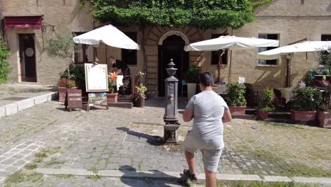 Tilt-down-reveal-shot-of-people-walking-on-a-cobblestone-street-in-Gradara,-Italy