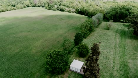 Small-white-house-in-a-vast-green-field-surrounded-by-trees,-Toulouse-countryside