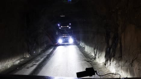 A-long-haul-logistics-truck-driver-waiting-patiently-as-a-fellow-driver-approaches-and-cautiously-navigates-past-in-a-tight-single-lane-tunnel,-Senja,-Norway