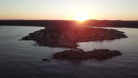 Aerial-drone-video-of-the-ocean-coastline-and-lighthouse-at-sunset-at-Nubble-Lighthouse-near-Cape-Neddick-and-York-Beach,-Maine,-United-States-of-America