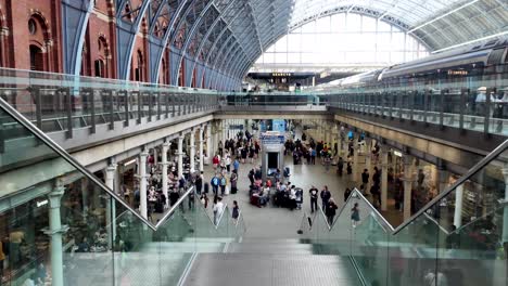 Kings-Cross-St-Pancras-Station-in-London,-with-travelers-and-visitors-strolling-through-the-station-area,-View-From-Upper-Level-Beside-Stairs