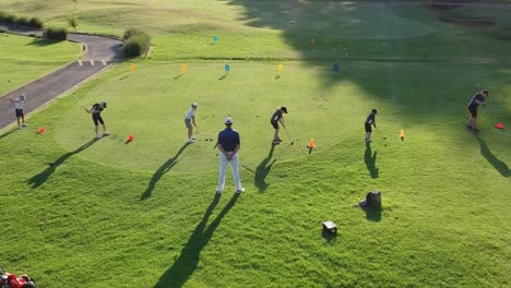 Niños-Siendo-Enseñados-Por-Un-Golfista-En-Un-Campo-De-Golf-Impecable,-Vista-Desde-Atrás-Por-Drones