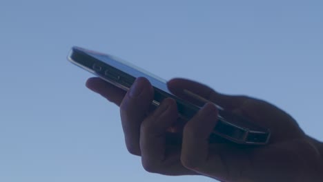 Handtippen-Auf-Smartphone-Mit-Transparenter-Hülle-Mit-Blauem-Himmel-Im-Hintergrund