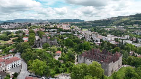 Aerial-view-of-Paços-dos-Duques-and-Guimarães-Castle-in-Portugal,-highlighting-historic-architecture-surrounded-by-lush-greenery