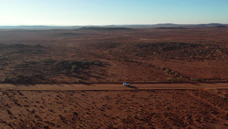 Aerial:-Drone-shot-tracking-parallel-to-a-white-vehicle-as-it-drives-along-a-dusty-outback-road-towards-Broken-Hill,-Australia