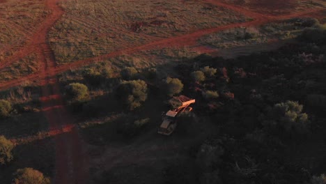 Vista-Aérea-De-Un-Vertedero-Con-Un-Remolque-De-Volcado-Hidráulico-Arrojando-Una-Carga-En-Un-Campo-Durante-La-Puesta-De-Sol