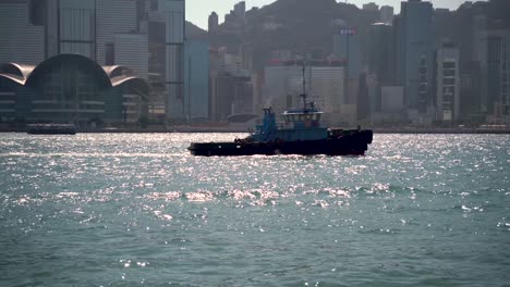 Boat-in-Victoria-Harbor-in-Hong-Kong-with-summer-sunlight-sparkling-and-glistening-against-the-reflection-of-ocean-waves,-China