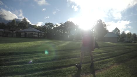 Marathon-athlete-hiking-and-walking-slow-through-village-on-a-grass-field-with-lens-flare-in-bush-jungle-dreamy-nature-of-Tanzania---slowmotion