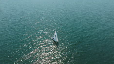 Aerial-establishing-view-of-a-white-sailboat-in-the-calm-Batltic-sea,-white-sailing-yacht-in-the-middle-of-the-boundless-sea,-sunny-summer-day,-wide-birdseye-done-shot-moving-forward