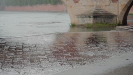 Wet-cobblestone-pavement-reflecting-light,-with-a-stone-bridge-and-river-in-the-background