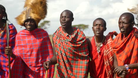 Massai-Stammeskrieger-Tanzen-Zu-Traditionellen-Liedern-Und-Musik-Mit-Straußen--Und-Löwenkopfbedeckungen-In-Der-Nähe-Der-Mara-Im-Masai-Mara-Nationalpark-In-Kenia-Und-Blasen-Horn