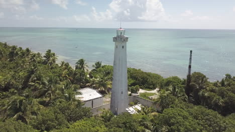 Drone-orbit-around-Lighthouse-in-Punta-Allen-Beach,-Mexico-with-birds-flying-above