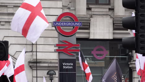 Banderas-Rojas-Y-Blancas-De-Saint-George,-Inglaterra,-Ondean-Alrededor-De-Un-Cartel-De-La-Estación-De-Tren-Y-Metro-De-Victoria-Durante-Una-Protesta-De-Extrema-Derecha