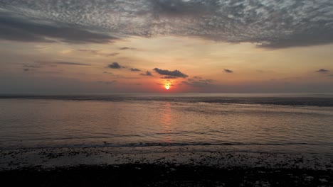 Glide-backward-along-the-beach-at-sunset-in-this-serene-drone-footage,-capturing-the-beauty-of-the-Gili-coastline-as-the-sun-dips-below-the-horizon