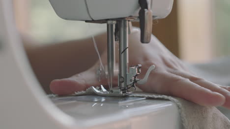 Tailor's-Hand-Sewing-Fabric-With-Her-Sewing-Machine-In-The-House---closeup-shot