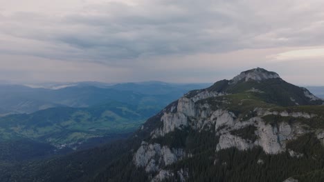 Aerial-view-showing-tall-mountains-covered-in-dense-coniferous-green-forests,-cloudy-day