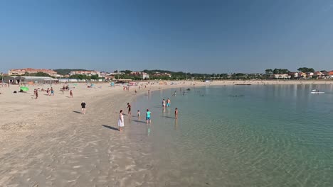 people-enjoying-a-morning-on-the-beach-of-crystal-clear-water,-sunbathing,-swimming,-walking,-canoeing,-european-holiday-town,-sunny-morning,-descriptive-panning