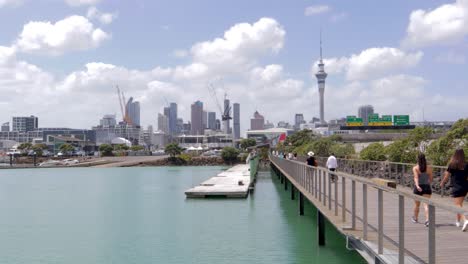 Auckland-city-view-in-background,-people-walking-on-westhaven-bridge-and-looking,-New-Zealand