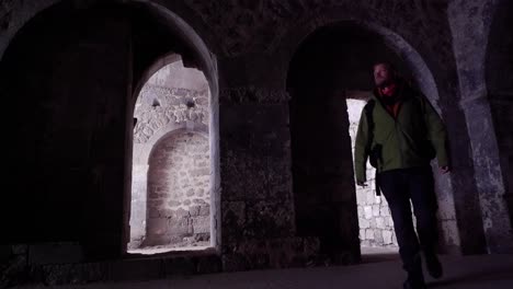 Man-in-rain-jacket-enters-medieval-church-through-arch-stone-door