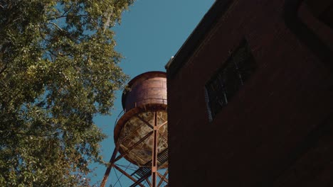 Alta-Y-Antigua-Torre-De-Agua-Rústica-En-El-Exterior-Revelada-Desde-Detrás-De-Un-Edificio