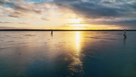 Two-windsurfers-surfing-on-frozen-lake-in-sunset